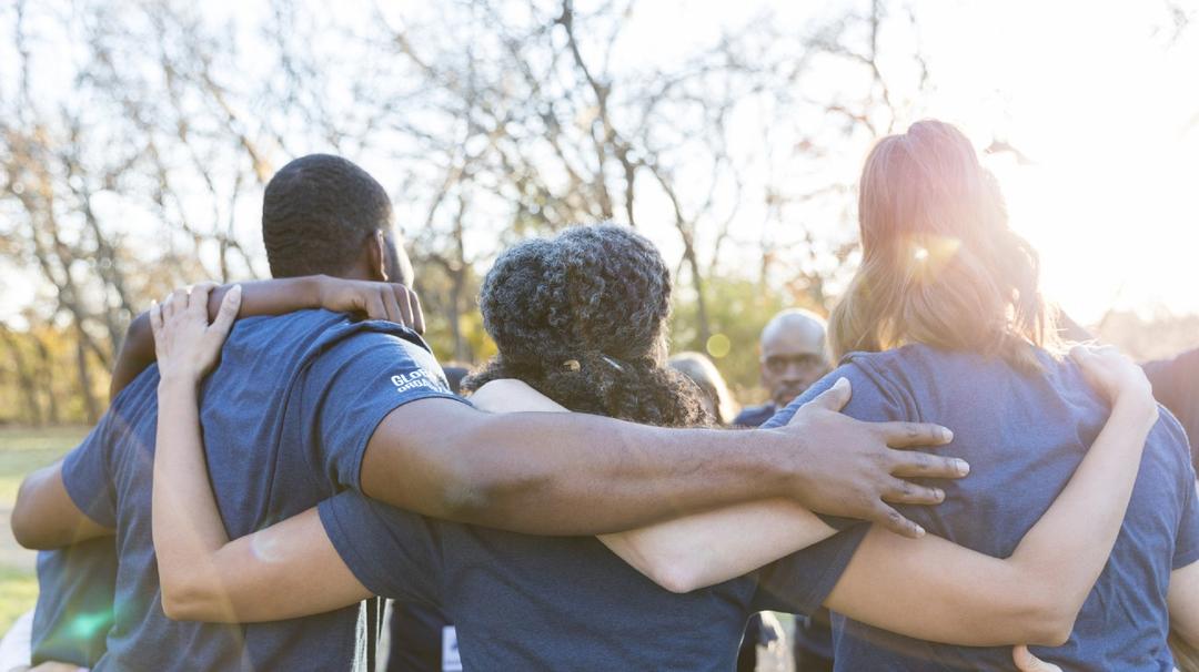 Group of men and women standing in a circle with their arms around each other.